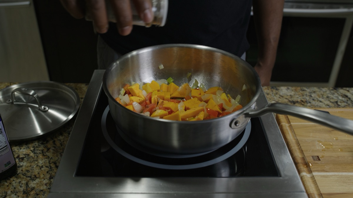 Seasoning sautéed onion, peppers, and squash in a pot