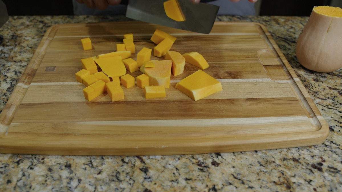 Cubing fresh squash on a wooden cutting board