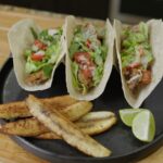 Three crispy oyster mushroom tacos with lettuce, cherry tomatoes, and ranch drizzle, served with fried burro bananas and lime