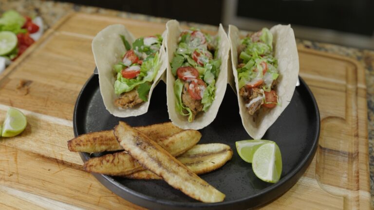 Three crispy oyster mushroom tacos with lettuce, cherry tomatoes, and ranch drizzle, served with fried burro bananas and lime