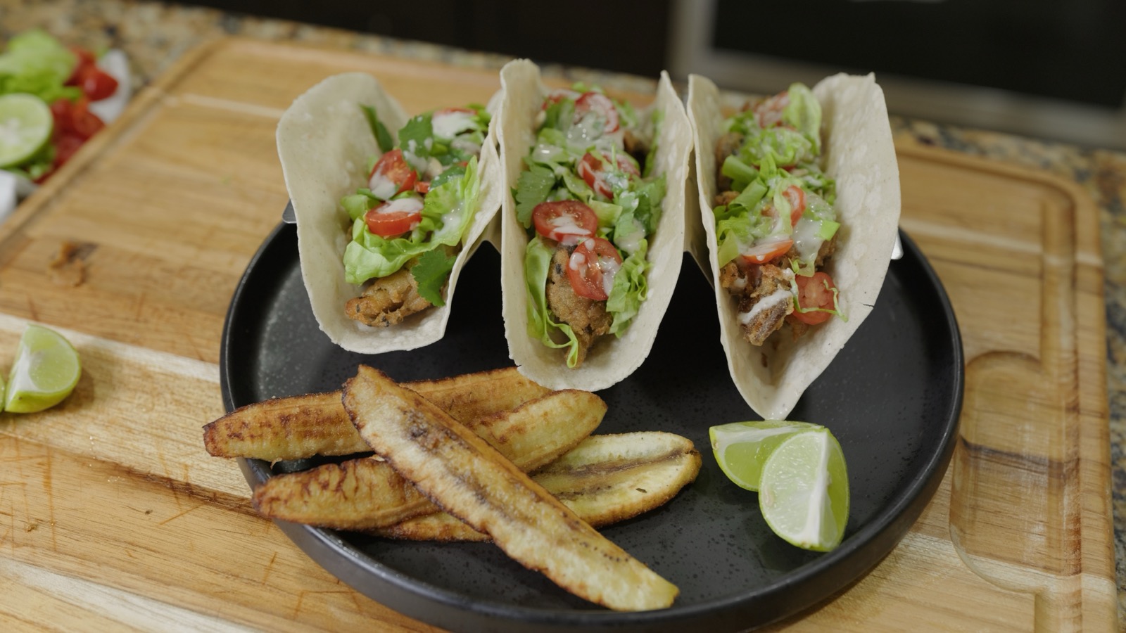 Three crispy oyster mushroom tacos with lettuce, cherry tomatoes, and ranch drizzle, served with fried burro bananas and lime